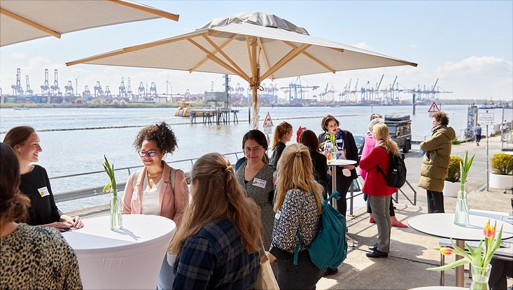 Gäste der Fokus: WissKomm Veranstaltung stehen vor der Kulisse des Hamburg Hafens an Stehtischen zusammen.