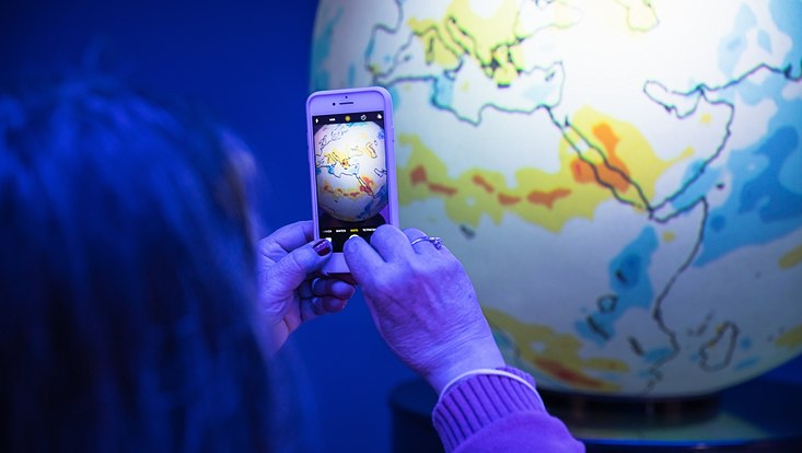 Eine Frau fotografiert mit ihrem Handy eine Weltkugel