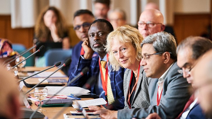 GUC 2023 Menschen, die in einer Reihe an Tischen sitzen. Vor jeder Person befindet sich ein Mikrofon. Auf den Tischen liegen Unterlagen und Smartphones.