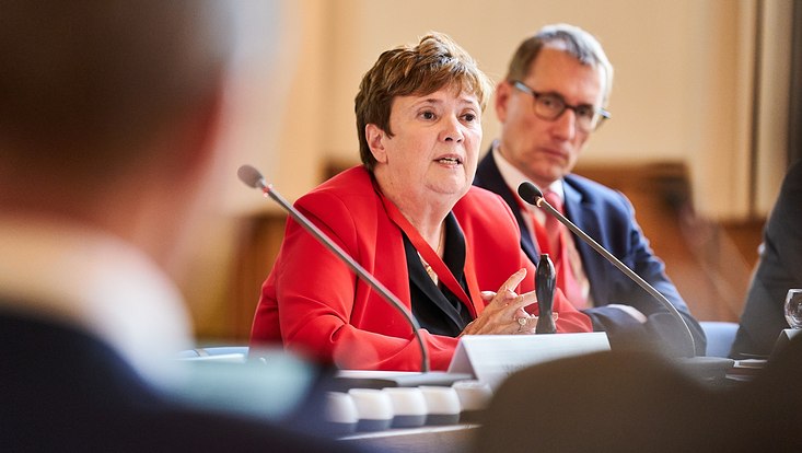 GUC 2023 Nahaufnahme einer Frau, die in ein Mikrofon spricht. Im Hintergrund sitzt ein Mann.