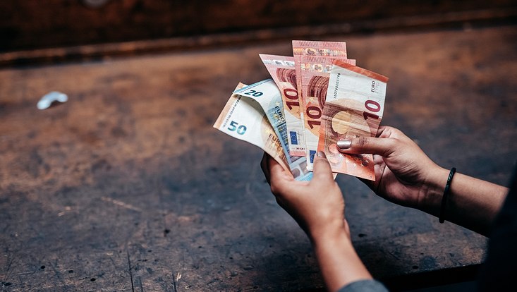Blick auf die Hände einer Person, die Geldscheine in der Hand hält.