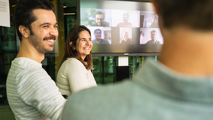 Hybrid event: people sitting together, more people can be seen in the background joining online