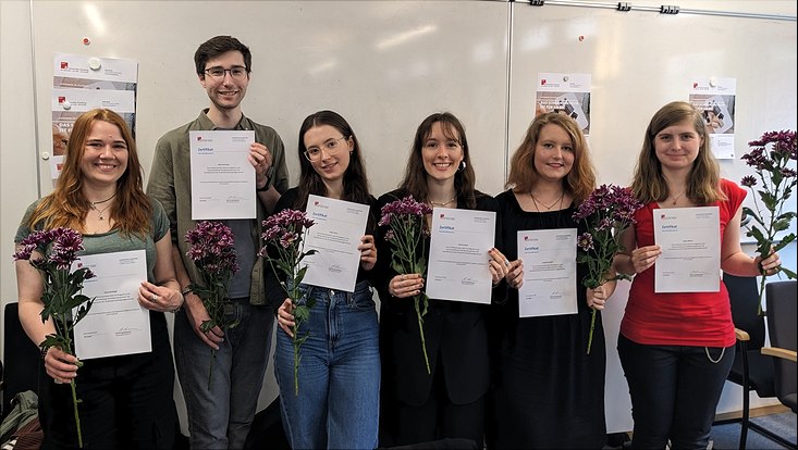 Studierende halten Zertifikate und Blumen