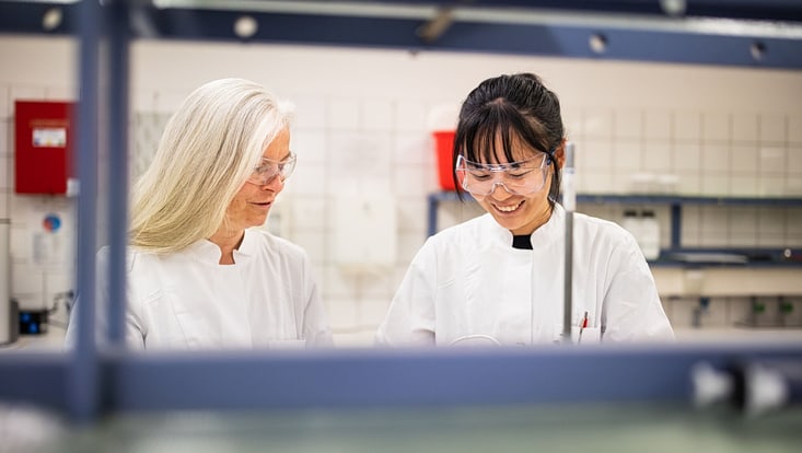Zwei Frauen in Arbeitskleidung in einer Laborsituation des Bereichs Lebensmittelchemie