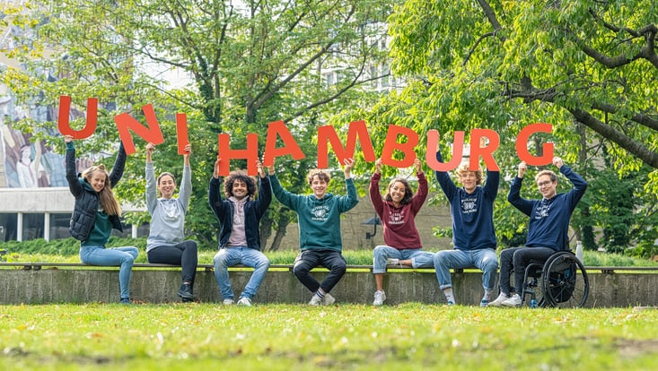 Unitag der Universität Hamburg Studierende sitzen auf dem Campus und halten Buchstaben, die "Uni Hamburg" schreiben,in die Luft