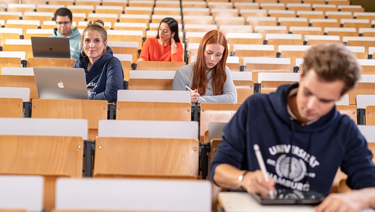 Blick in einen gestuften Hörsaal mit mehreren Studierenden.