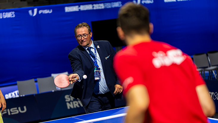 Zwei Männer spielen Tischtennis vor blauem Hintergrund