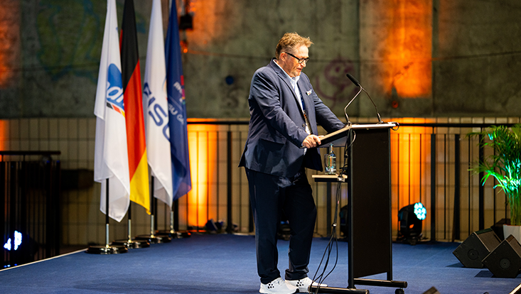 Mann auf Bühne am Sprecherpult im Hintergrund Flaggen