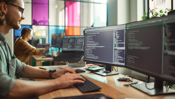männlicher Programmierer am Computer mit zwei Bildschirmen