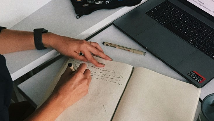 Hände schreiben mit Stift in Notizbuch vor Laptop