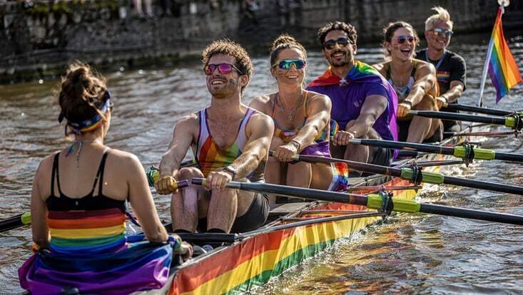 Eine bunte Gruppe Ruderer*innen in einem Regenbogen-Ruderboot