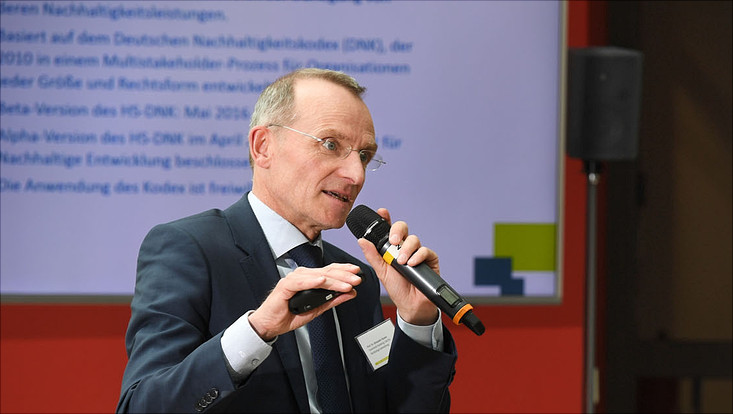 Prof. Alexander Bassen mit Mikrofon in der Hand erläutert den Hochschul-DNK