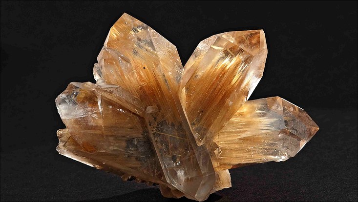 Weißlicher Bergkristall, in dem kleine, goldene, längliche Nadeln des Minerals Rutil eingeschlossen sind.