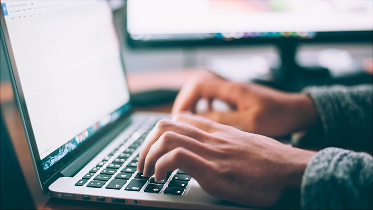 Person schreibt an einem Laptop. Großaufnahme von den Händen, die gerade auf der Tastatur tippen.