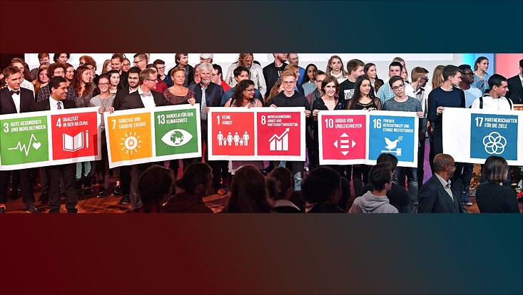 Studierende halten während der Immatrikulationsfeier SDG-Symbole hoch