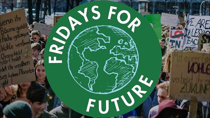 Das Logo der Fridays for Future vor dem Hintergrund streikender Menschen mit Plakaten.