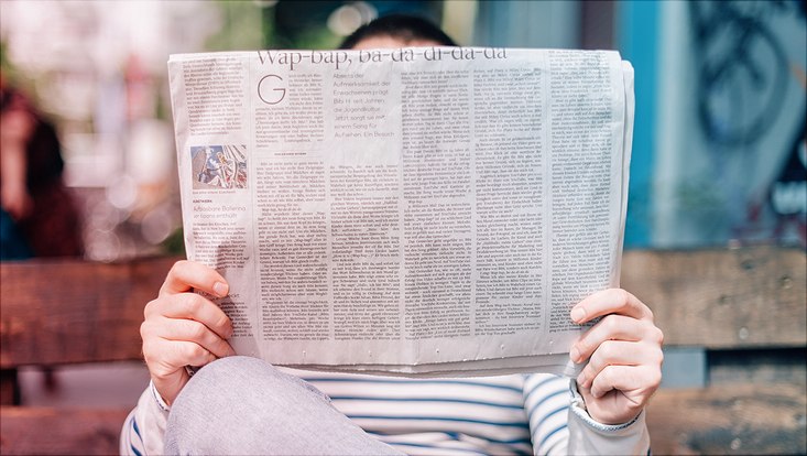 man sitting on bench reading newspaper