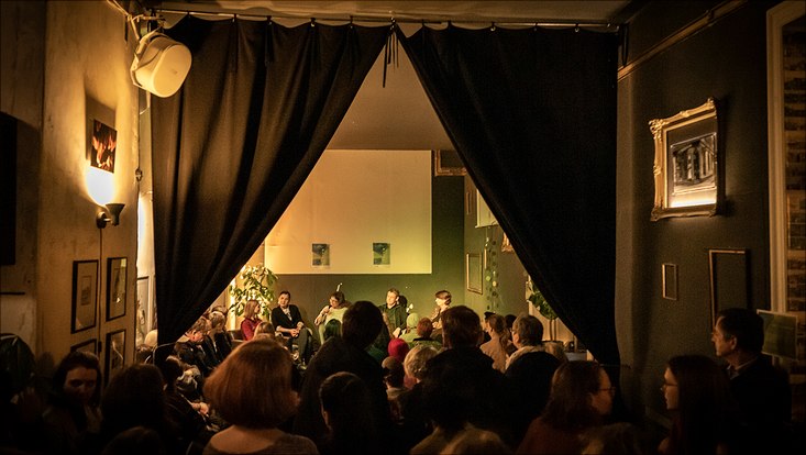 HRA Salon Menschen stehen und sitzen in der Bar verteilt und lauschen der Diskussion.
