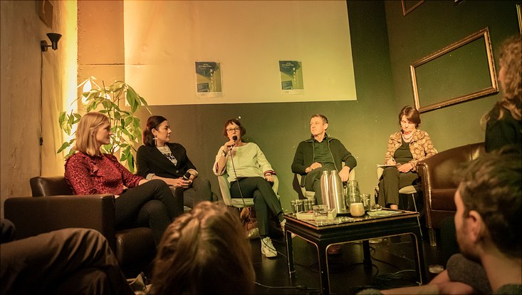 HRA Salon Die Podiumsgäste sitzen vorne und sprechen in ein Mikrofon.
